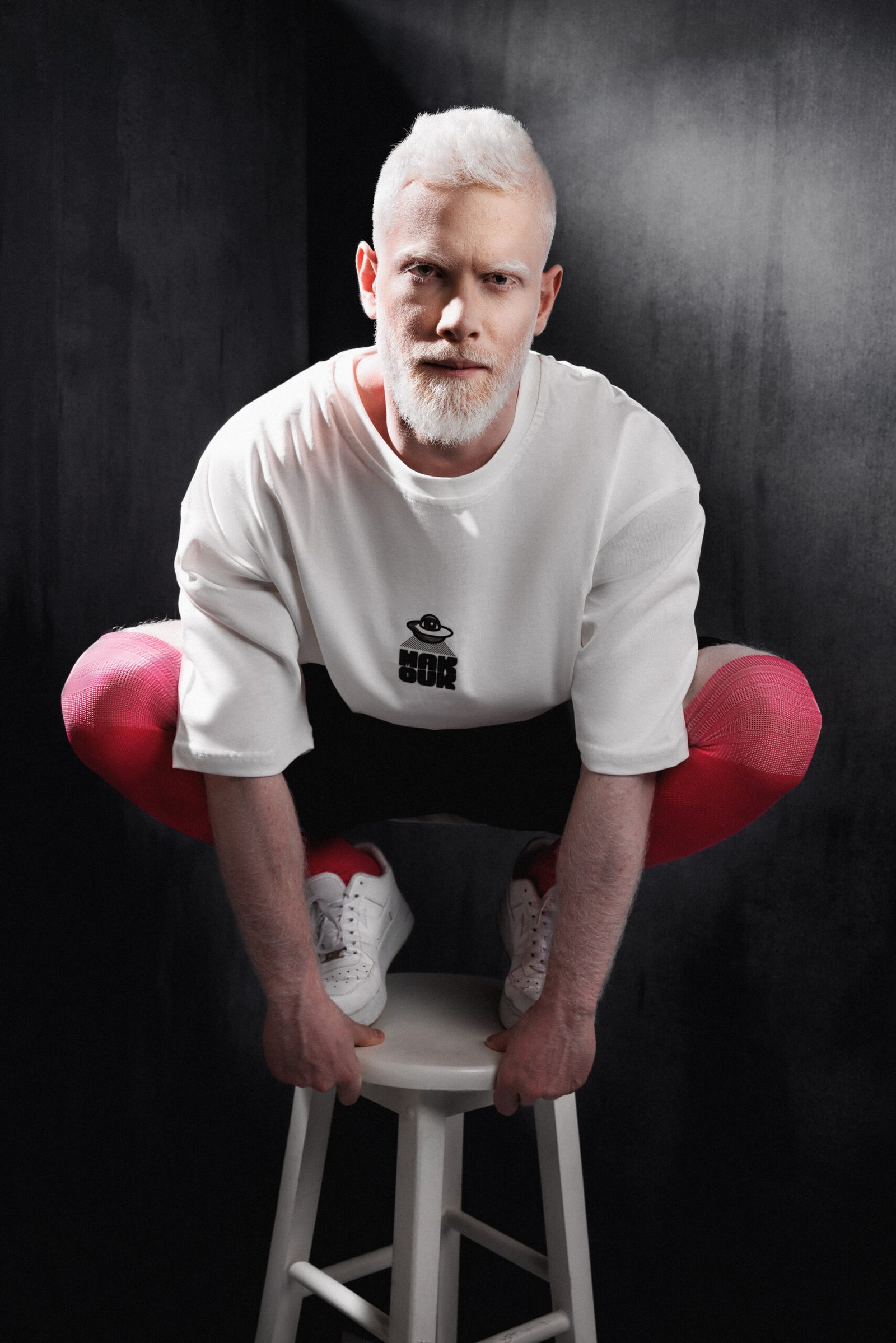 Model in white Makouk t-shirt and red tights squatting on stool. Designed by Mohamad Ali Makouk for Makouk Studios.
