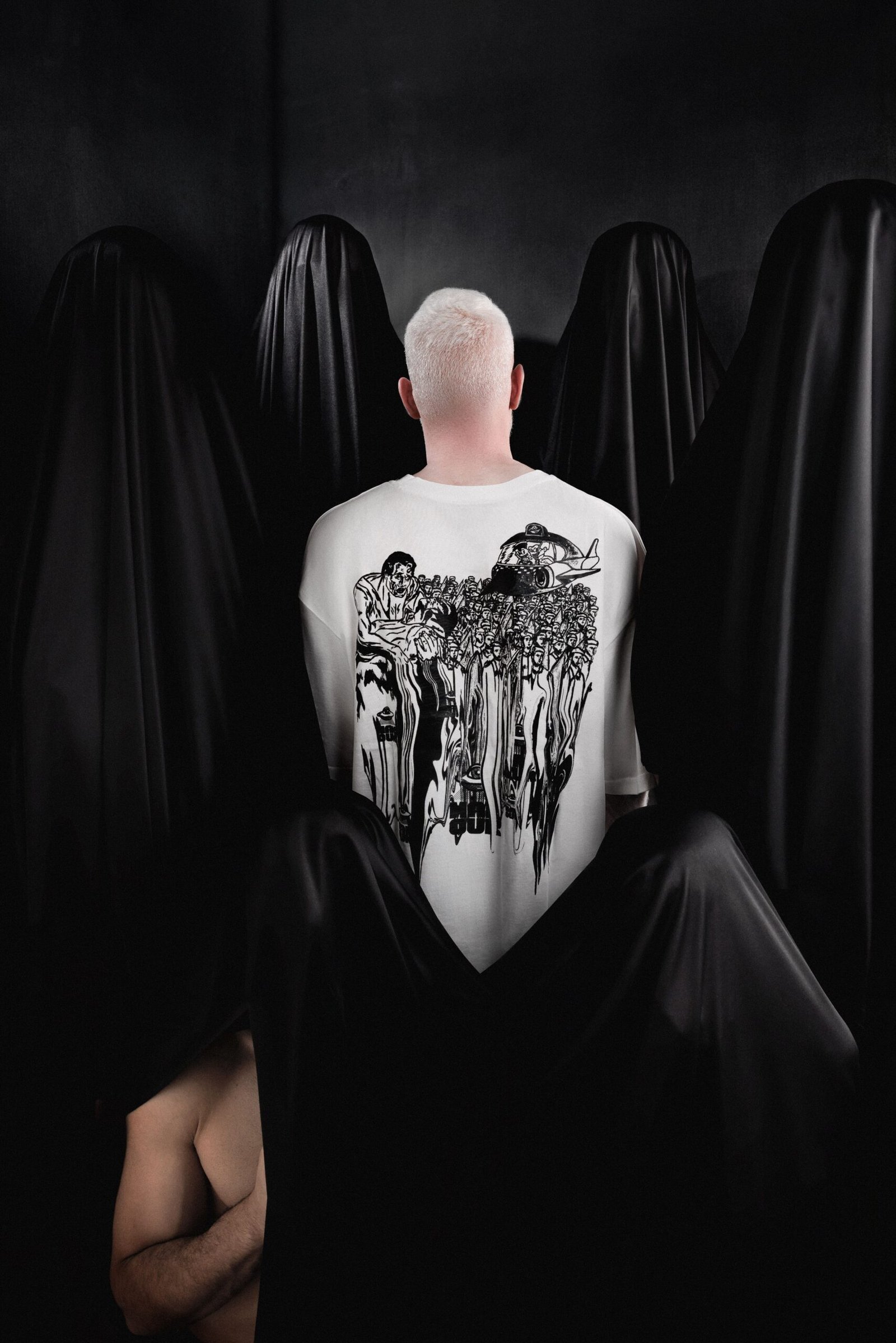 Male model wearing white Makouk Studios t-shirt with black illustration of men marching in conformity, from Macho Meltdown Collection by Mohamad Ali Makouk.